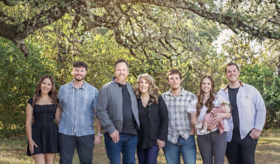 Jason Brooks and his family, eight adults and a baby, standing together under an oak tree